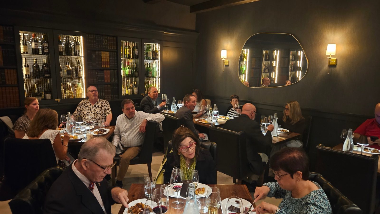 A full dining room at Enology Wine Bar and Bistro during the September benefit dinner, guests at wooden tables with the lit wine library behind them