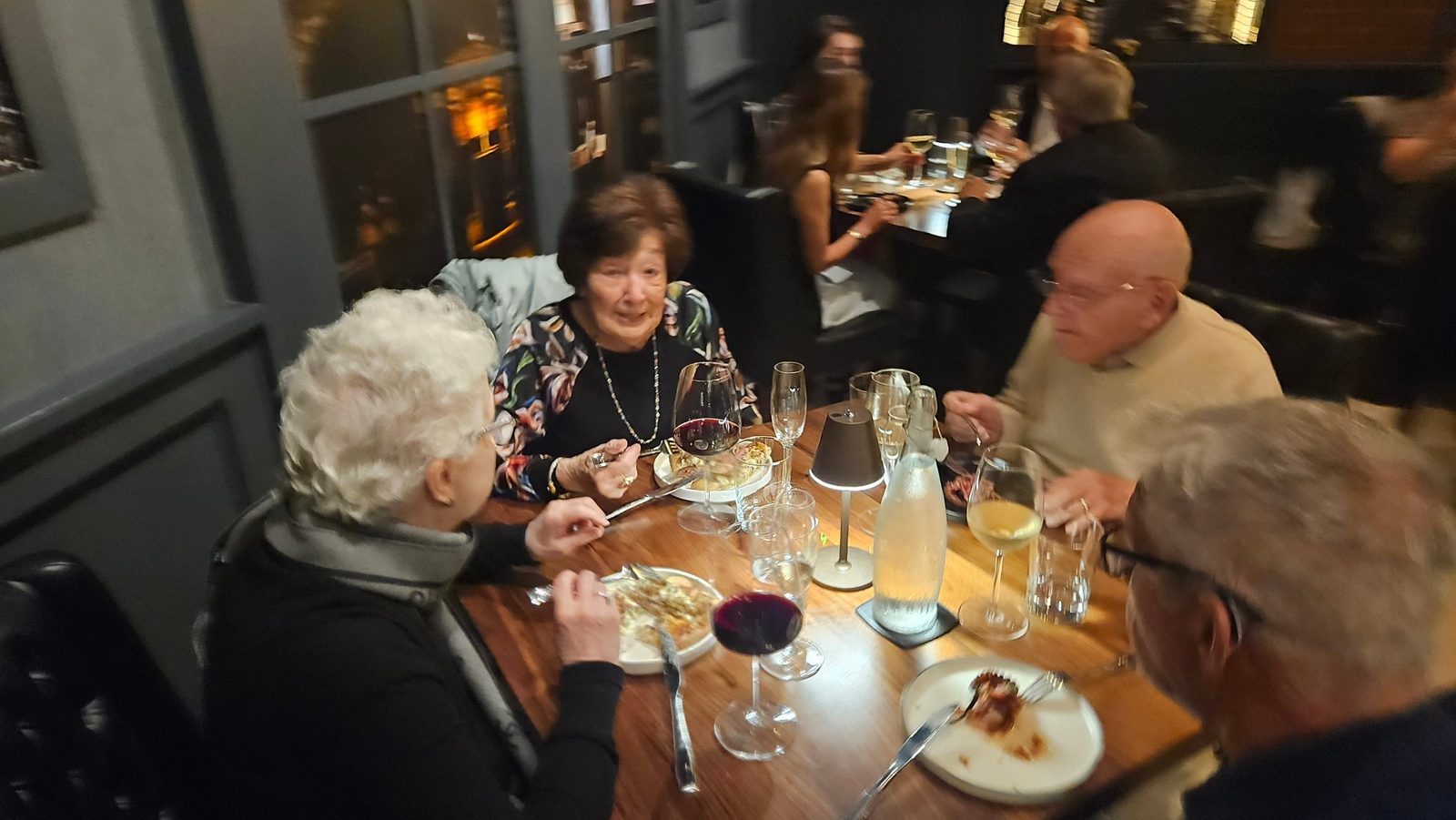Four guests around a wooden table at Enology, mid conversation with red and white wine poured