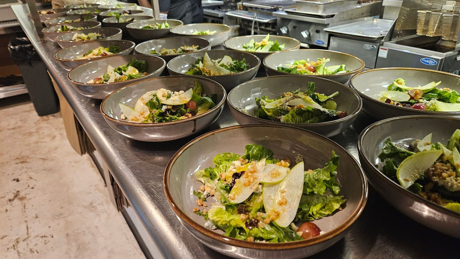 A long row of Waldorf salads plated with apple, pickled grapes, walnuts and blue cheese waiting on the kitchen pass at Enology