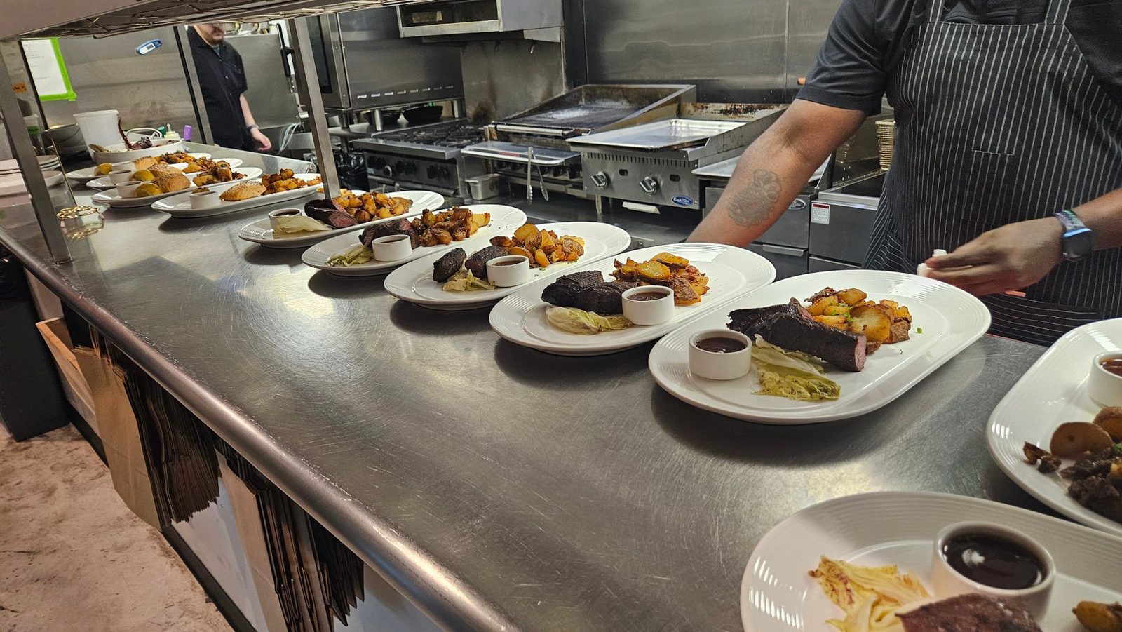 Plates of hanger steak with bistro sauce, radicchio and smashed crispy potatoes lined along the kitchen pass at Enology