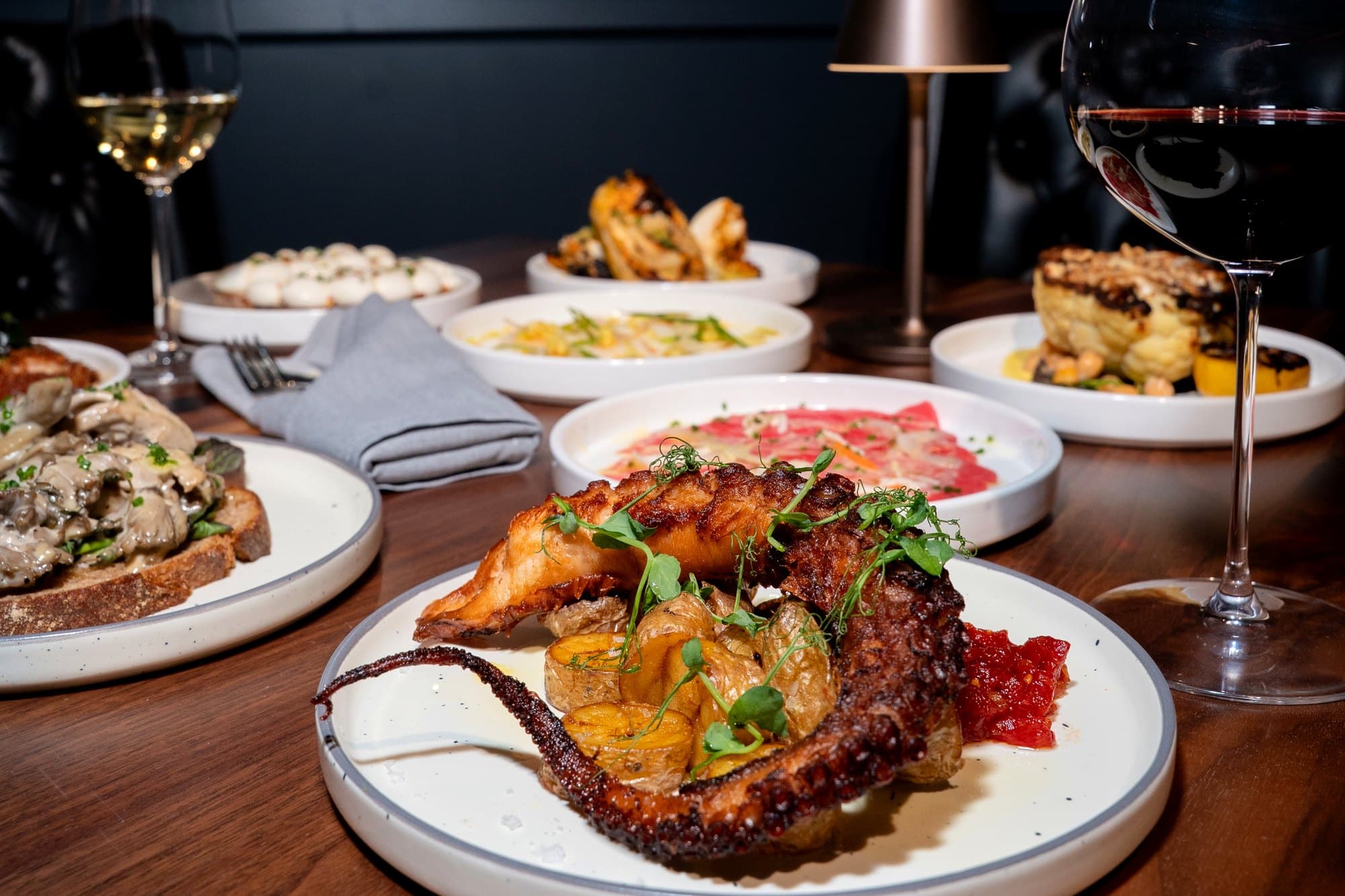 A spread of small plates with glasses of red and white wine on a warm-lit table at Enology