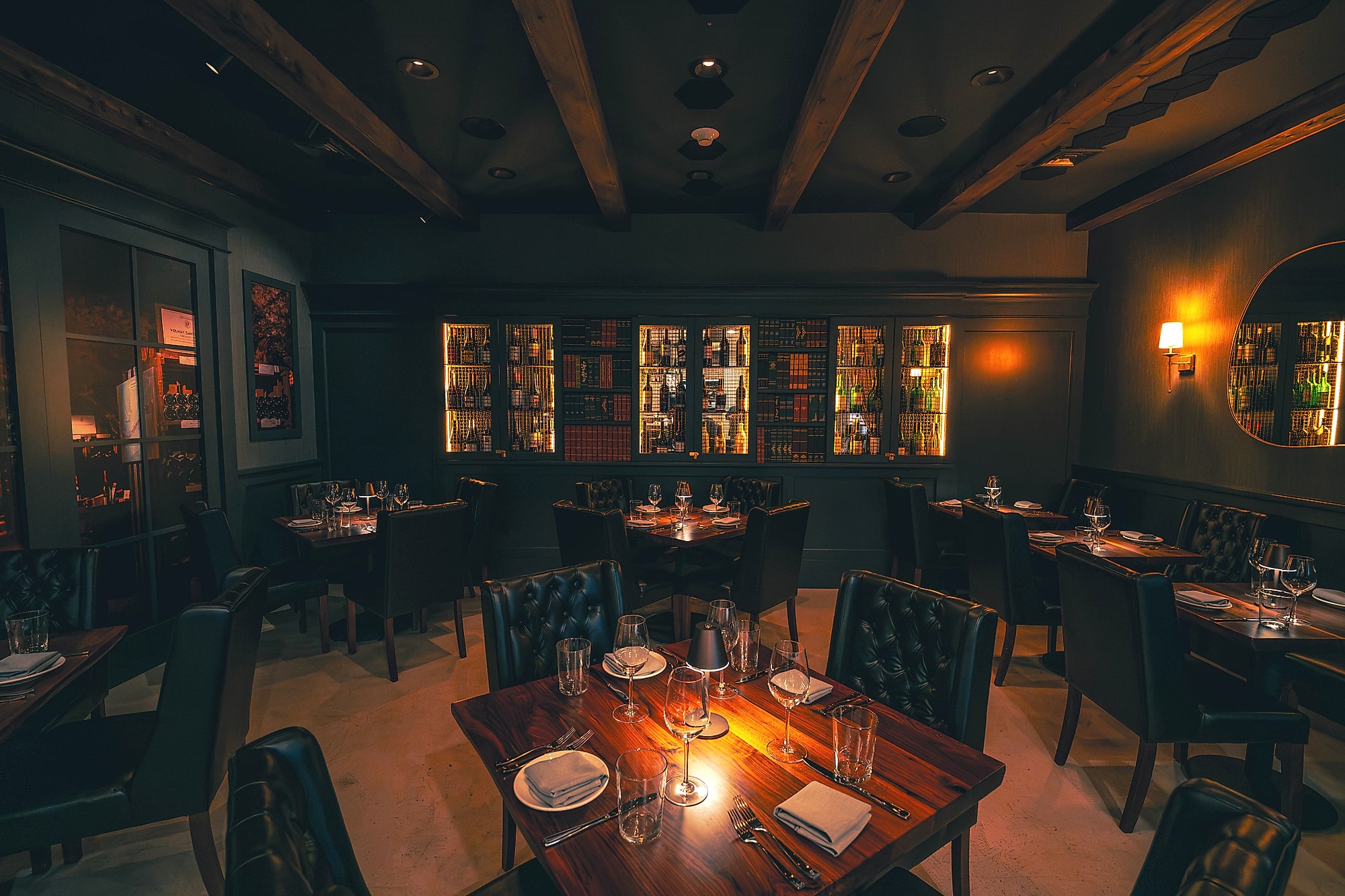 The Enology dining room at evening, walnut tables set with stemware beneath the backlit wine library