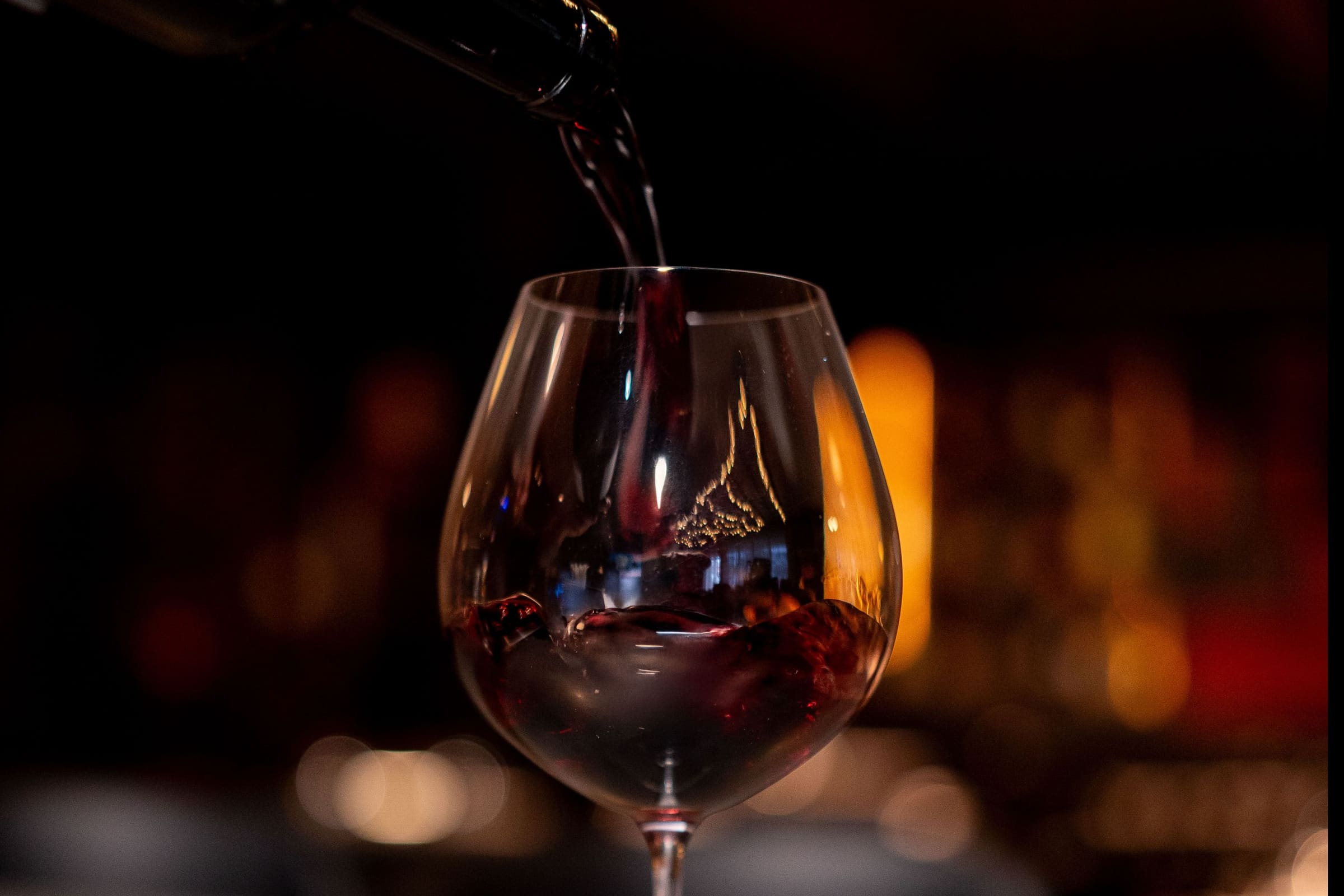 Red wine pouring into a glass in the warm low light of the bar at Enology