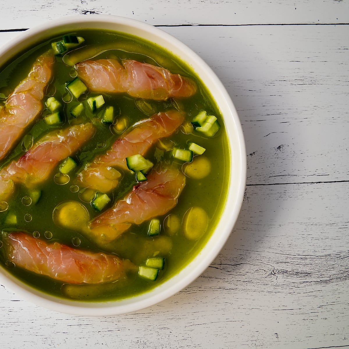 Market aguachile, thin slices of raw fish in a bright green broth with diced cucumber