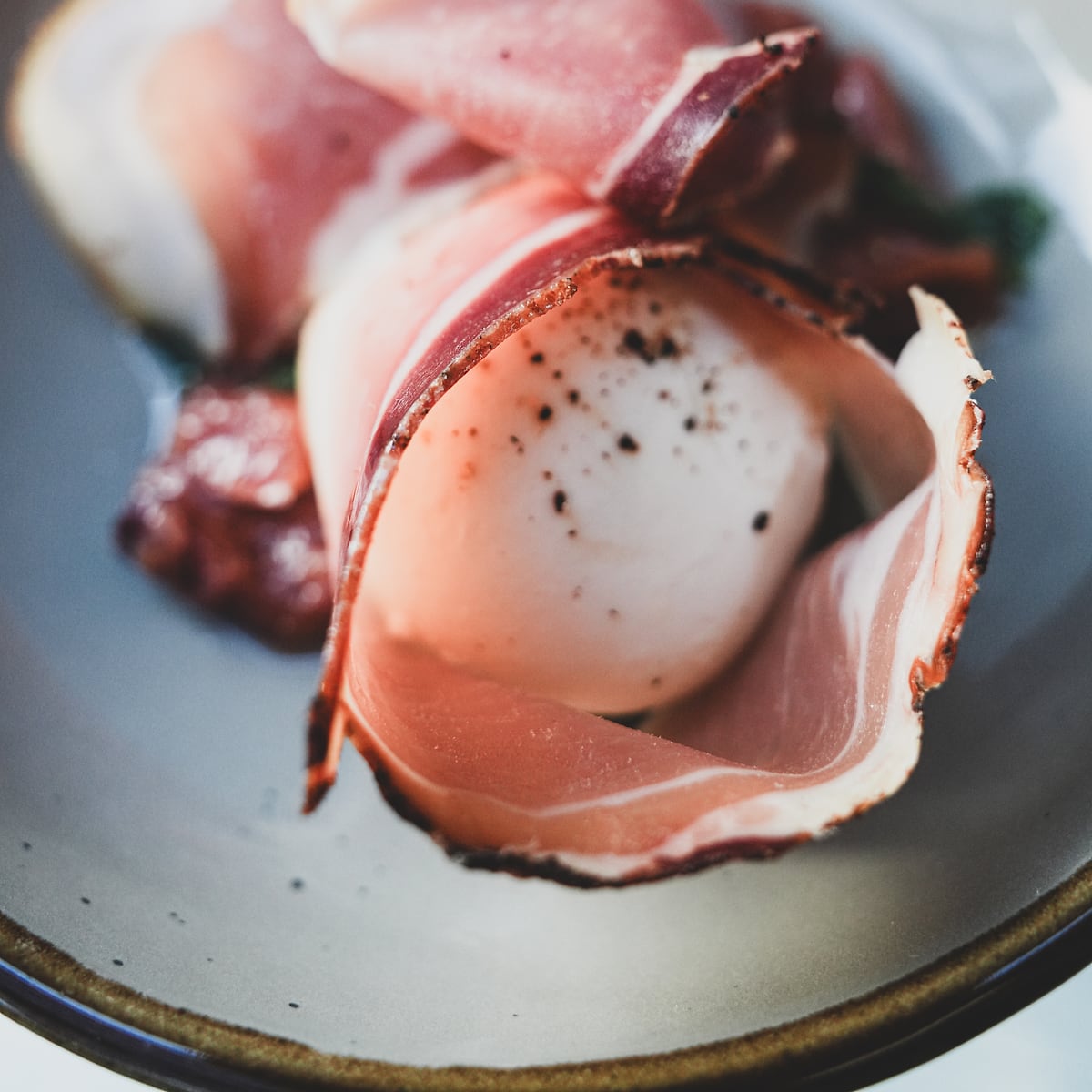 Burrata draped with prosciutto and cracked black pepper