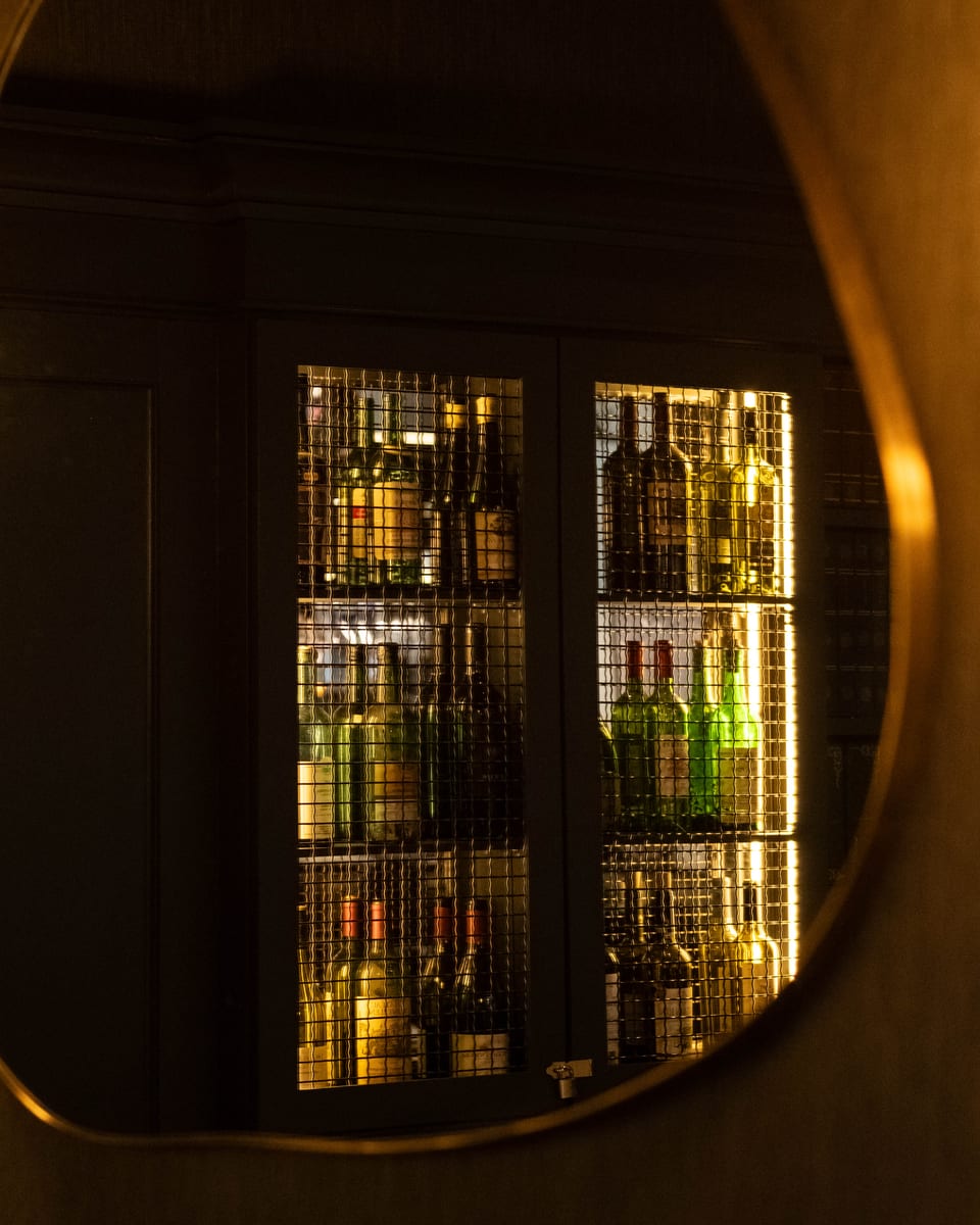 The lit bottle cabinets reflected in a brass-framed mirror