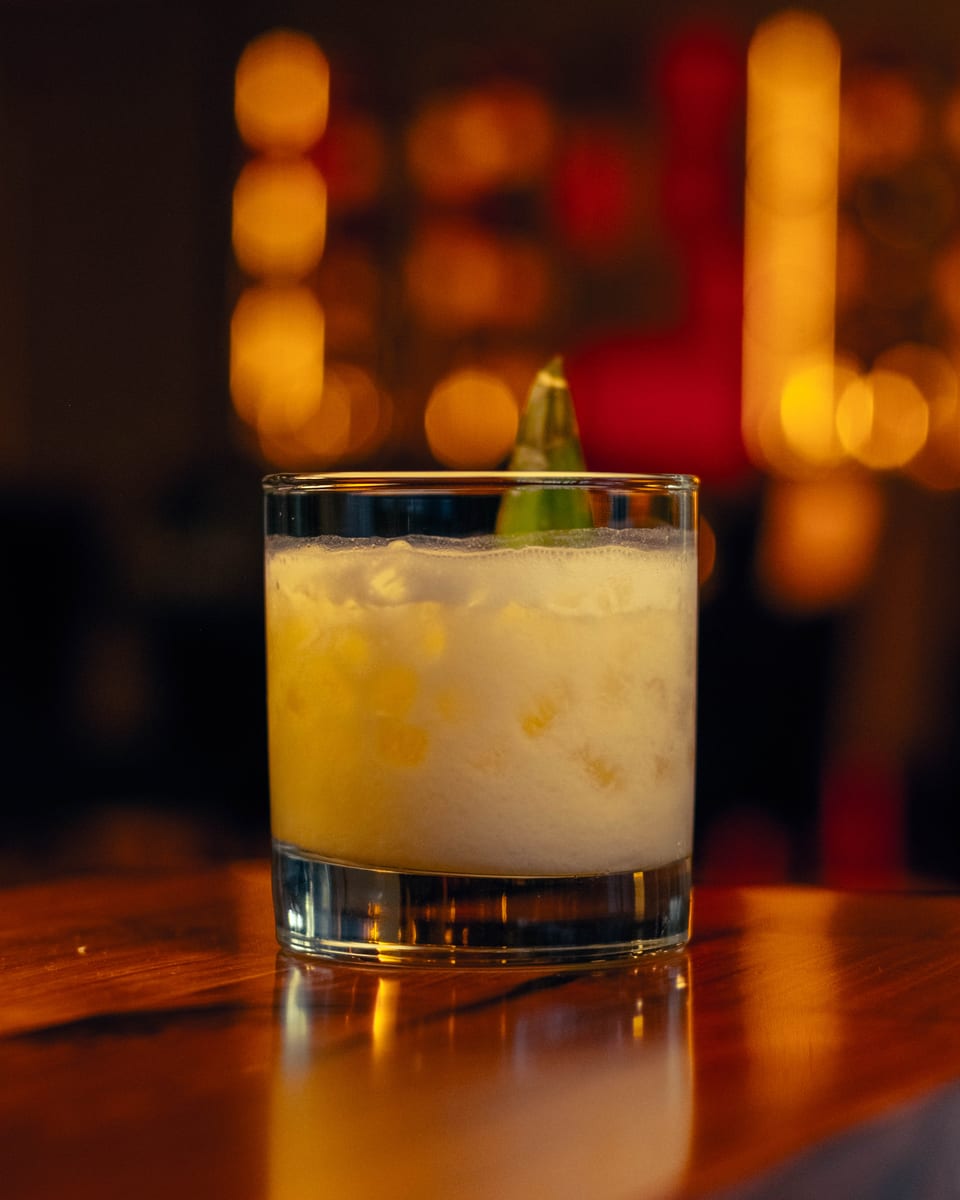 A frothy cocktail over crushed ice, finished with a green leaf garnish