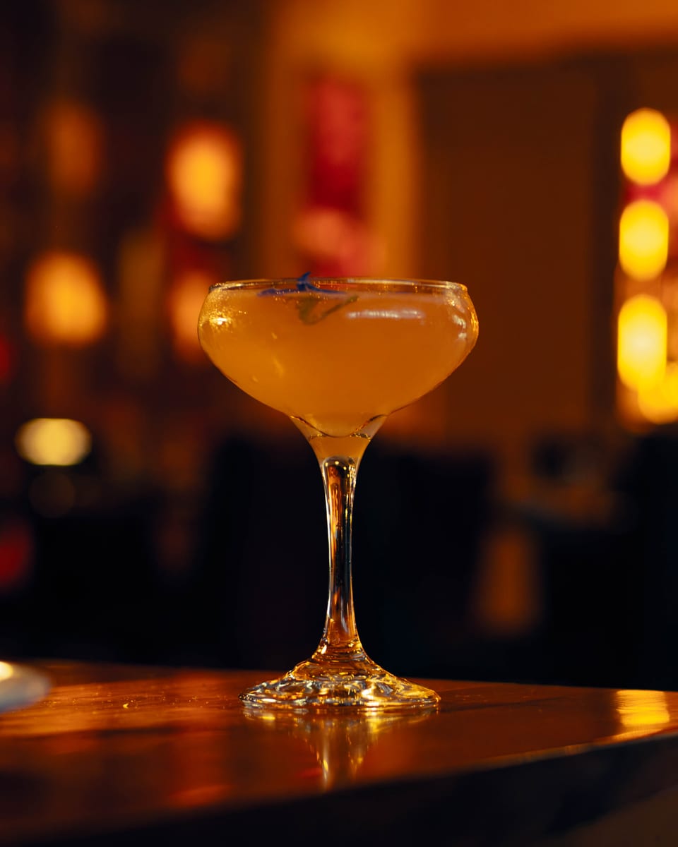 A coupe cocktail garnished with a single blue cornflower