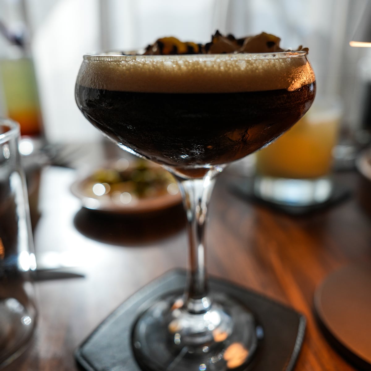 An espresso martini in a coupe, capped with a thick crema