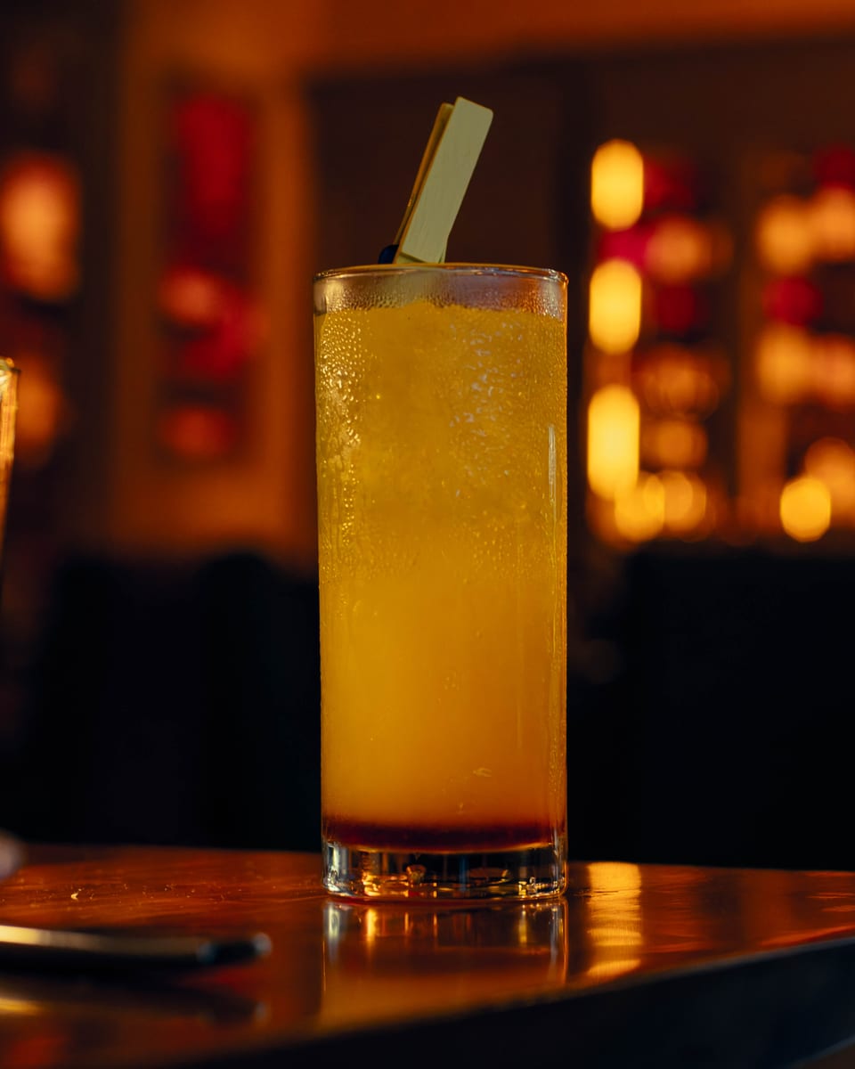 A tall amber highball over ice against the glow of the bar