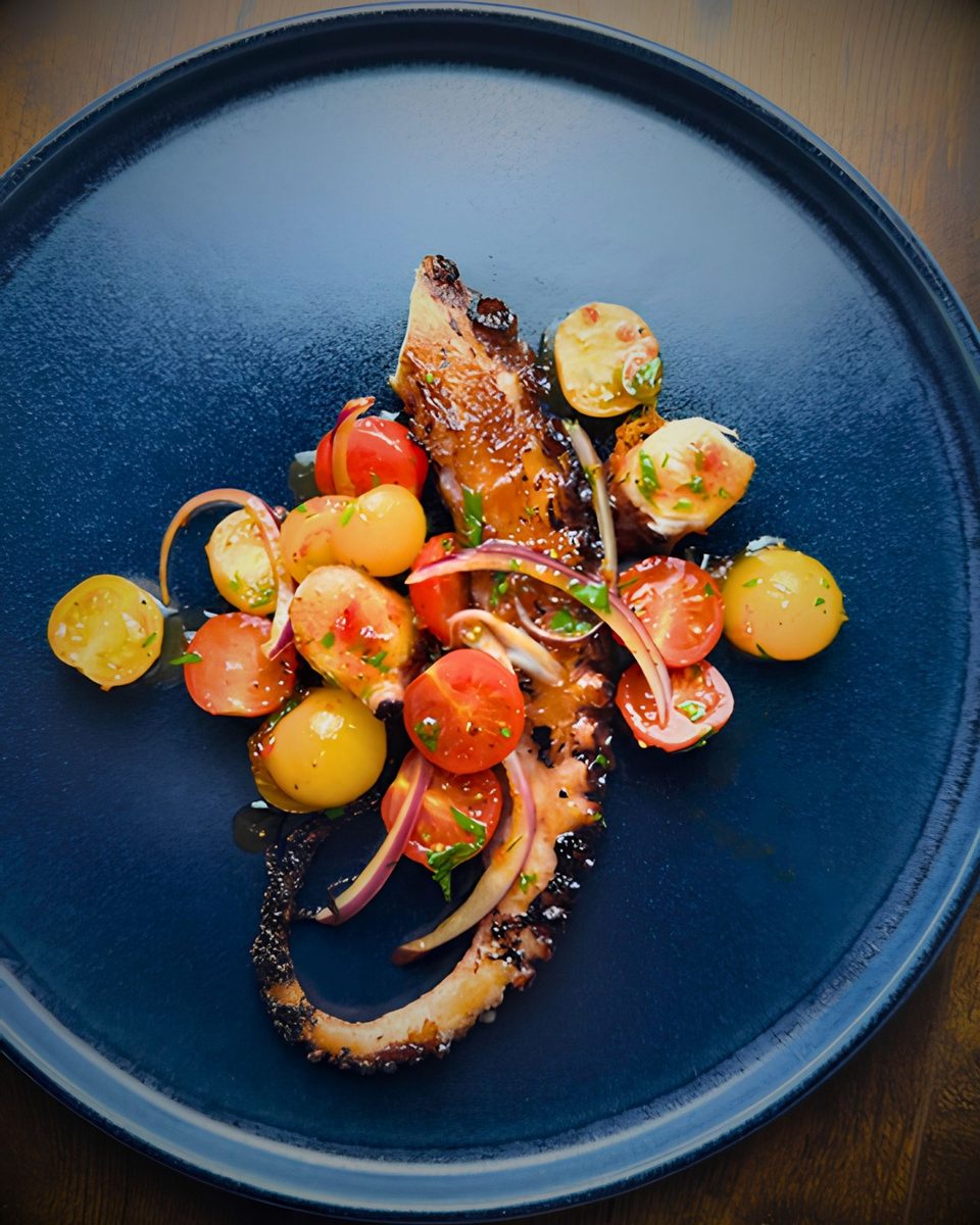 Grilled octopus with a cherry tomato and red onion salad on a navy plate