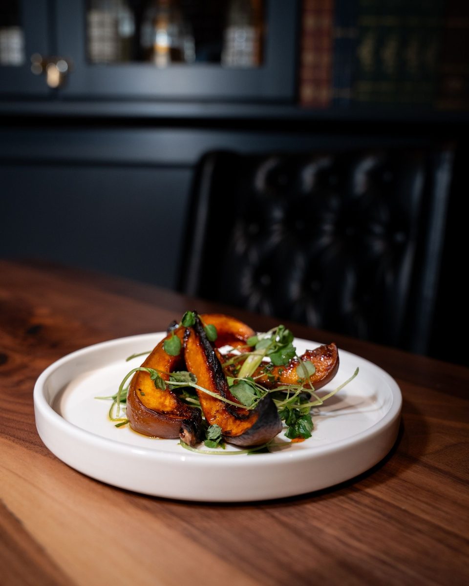 Roasted squash wedges with pea shoots and a chili glaze on a white plate
