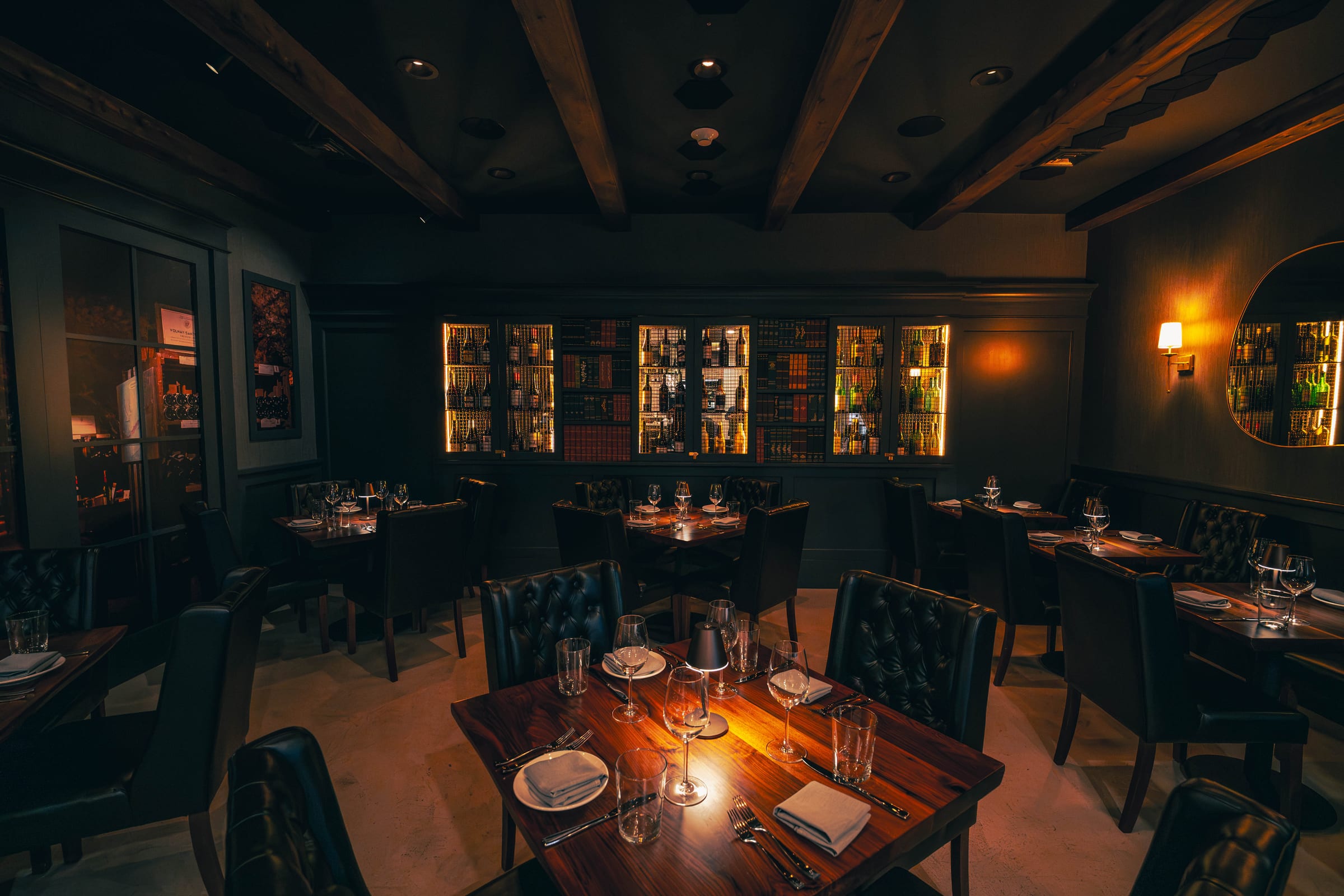 The Enology dining room at evening, walnut tables set beneath the backlit wine library
