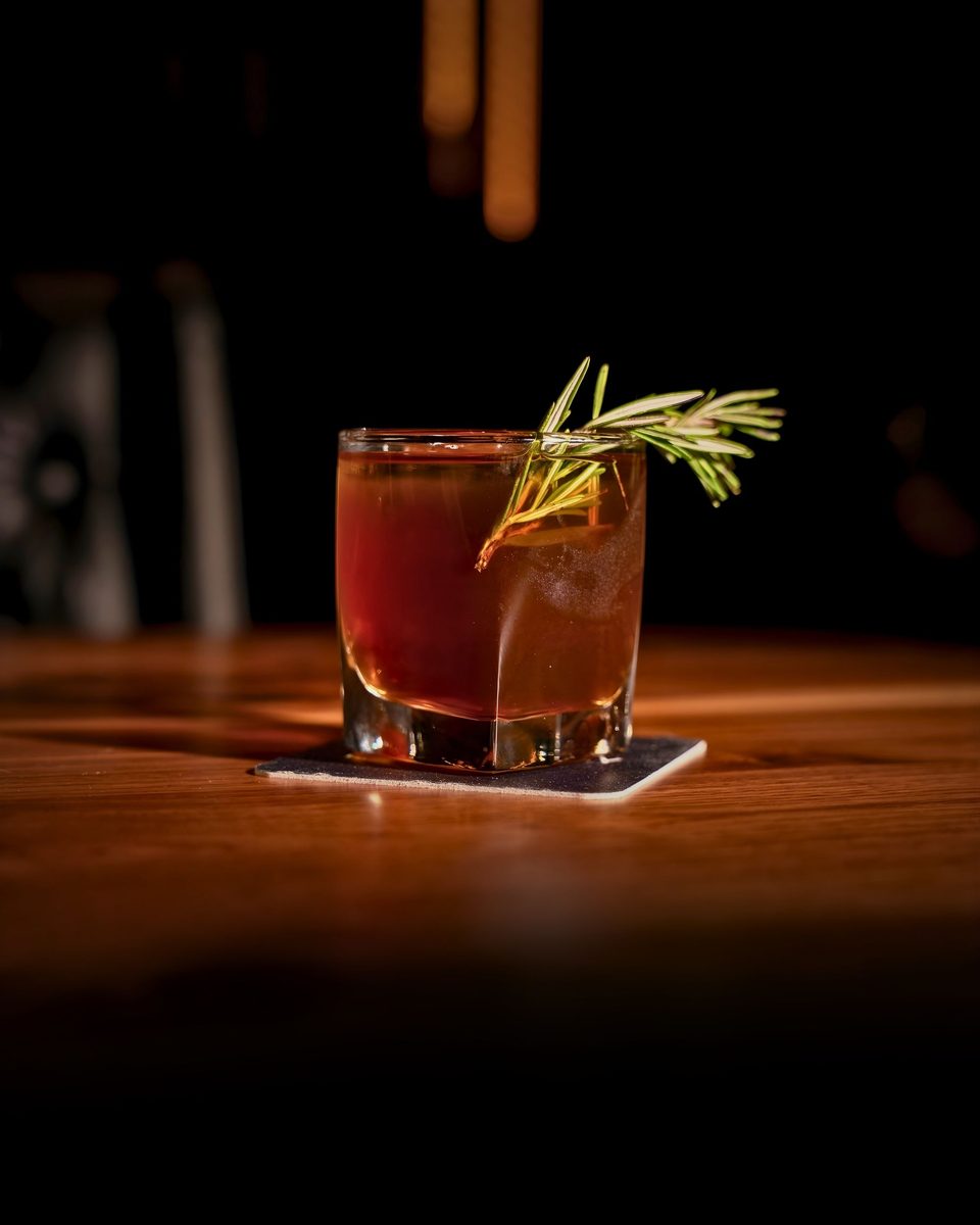 An amber cocktail garnished with fresh rosemary