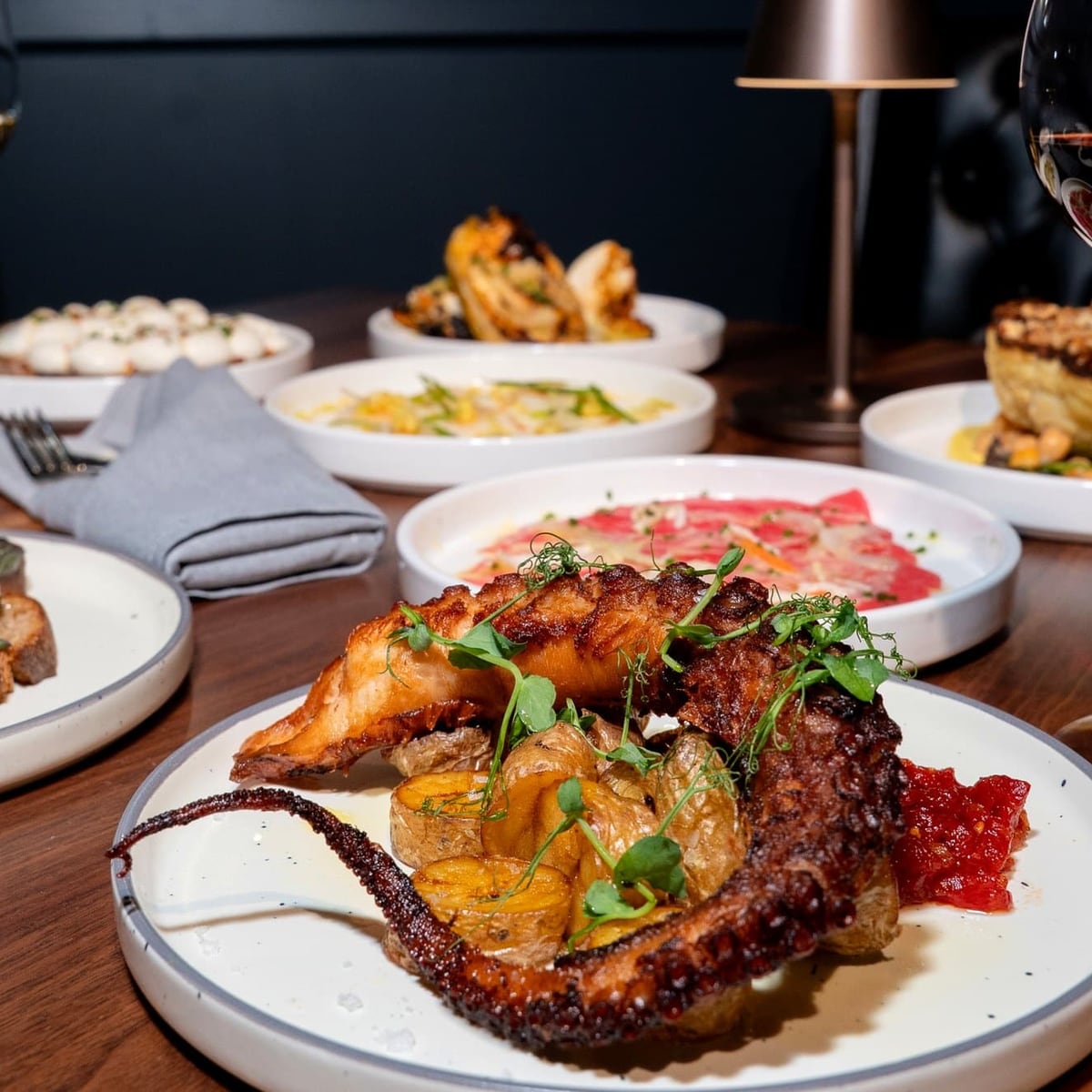 A spread of small plates with glasses of red and white wine on a warm-lit table