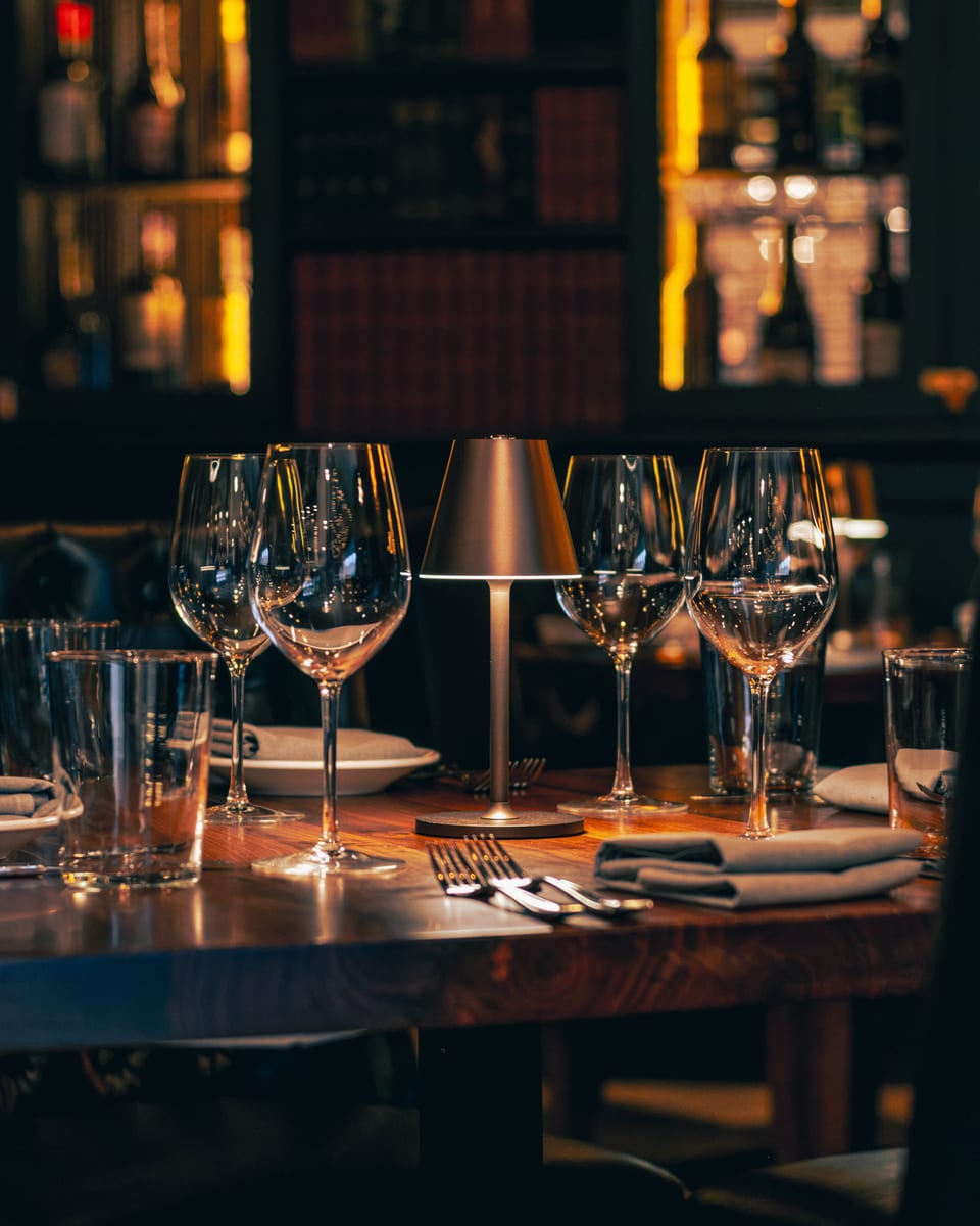 Wine glasses and folded napkins set along a walnut table before service at Enology