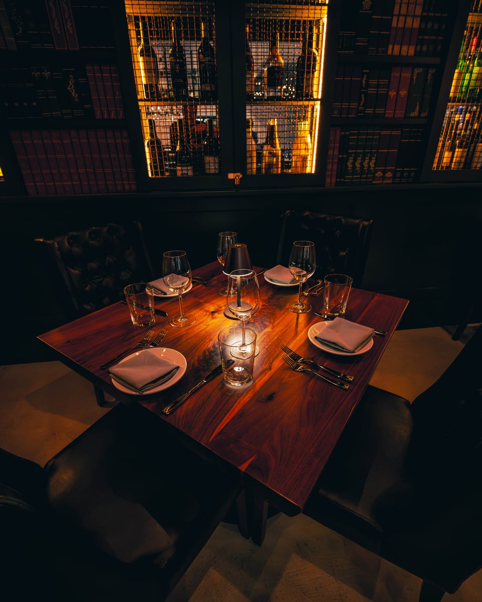 A table for four set with stemware and candlelight beneath the backlit wine library