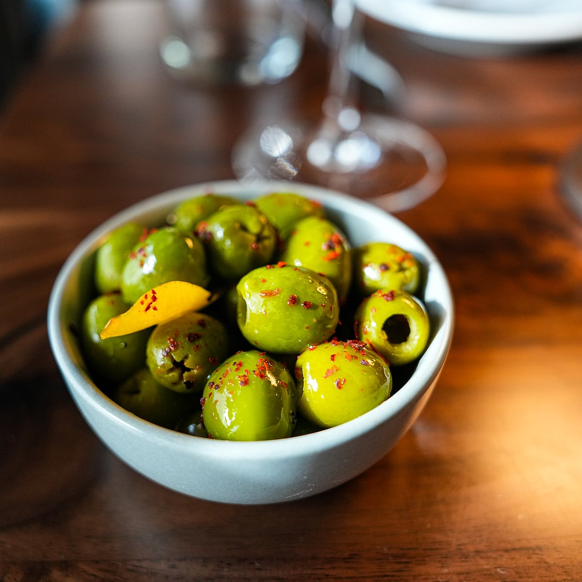 Warm marinated olives with chili and citrus peel in a pale ceramic bowl
